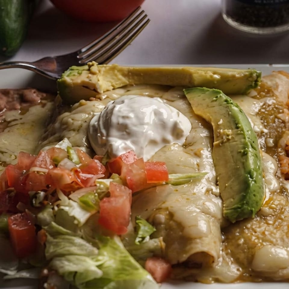 Mexican platter with cheese-covered enchiladas, avocado, sour cream, pico de gallo, refried beans, and Spanish rice.