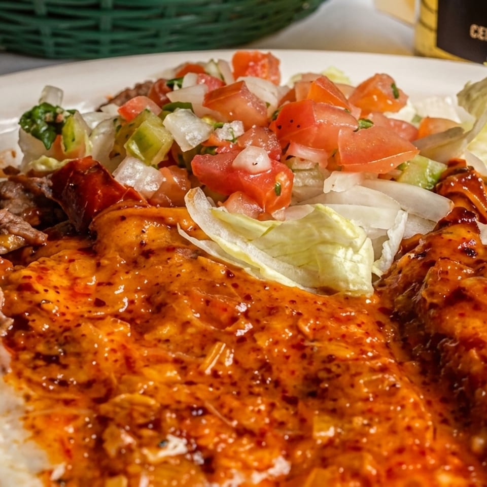 Enchiladas covered in red sauce with grilled meat, lettuce, and fresh tomato-onion salsa on a plate.