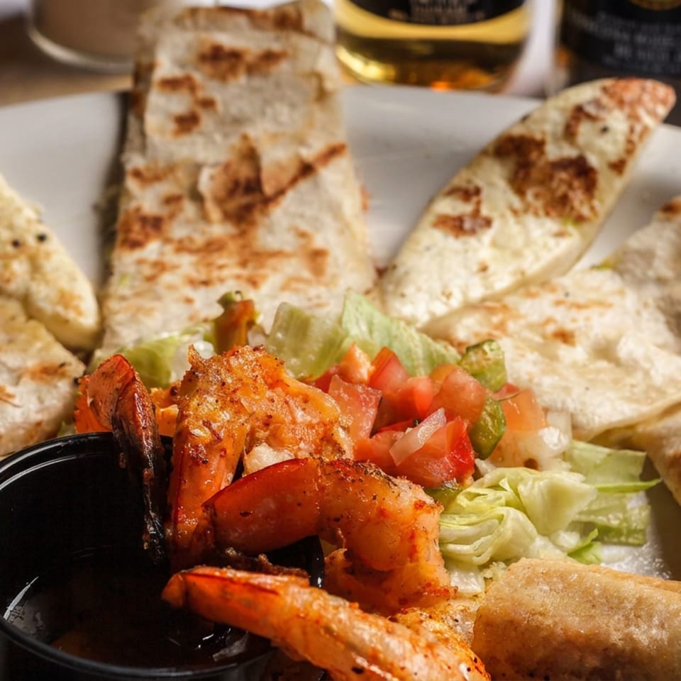 Assorted grilled quesadillas and crispy taquitos surround seasoned shrimp, lettuce, pico de gallo, and dipping sauces.