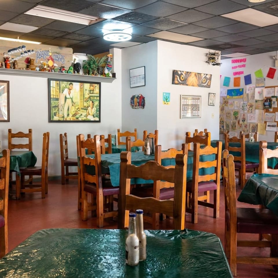 Colorful Mexican restaurant dining room with wooden chairs, teal tablecloths, cultural artwork, and festive wall decorations.