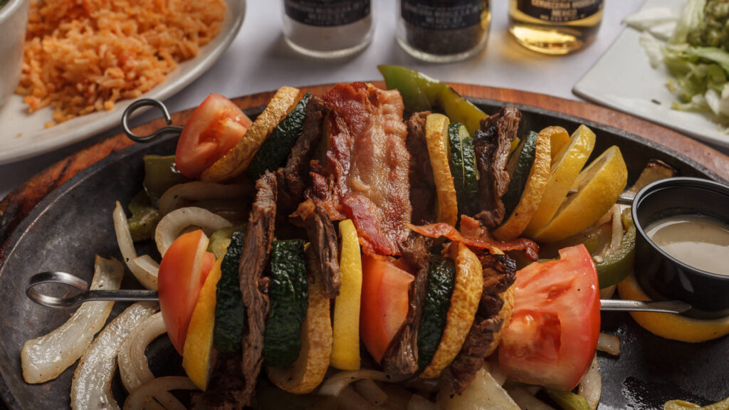 brochetas with sliced vegetables grilled onions and a cup with sauce