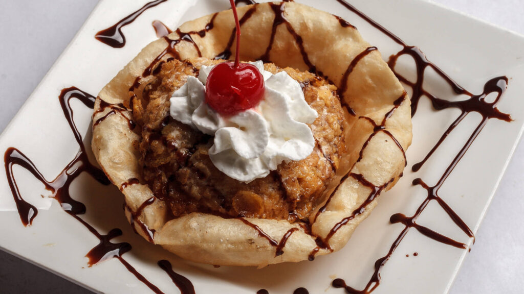 fried ice cream in a tortilla like a cone whip cream and cherry on top, plate decorated with chocolate