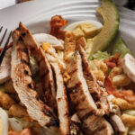 grilled chicken eggs sliced avocado lettuce bacon green vegtables in the bottom