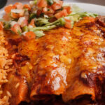 three wnchiladas cover with sauce melted cheese refied beams rice pico de gallo lettuce