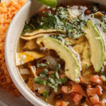 bowl of soup with beans avocado tortilla chips rice on the side of the bowl